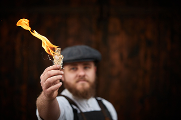Mann mit Schiebermuetze haelt brennenden Frankenzuende in die Kamera